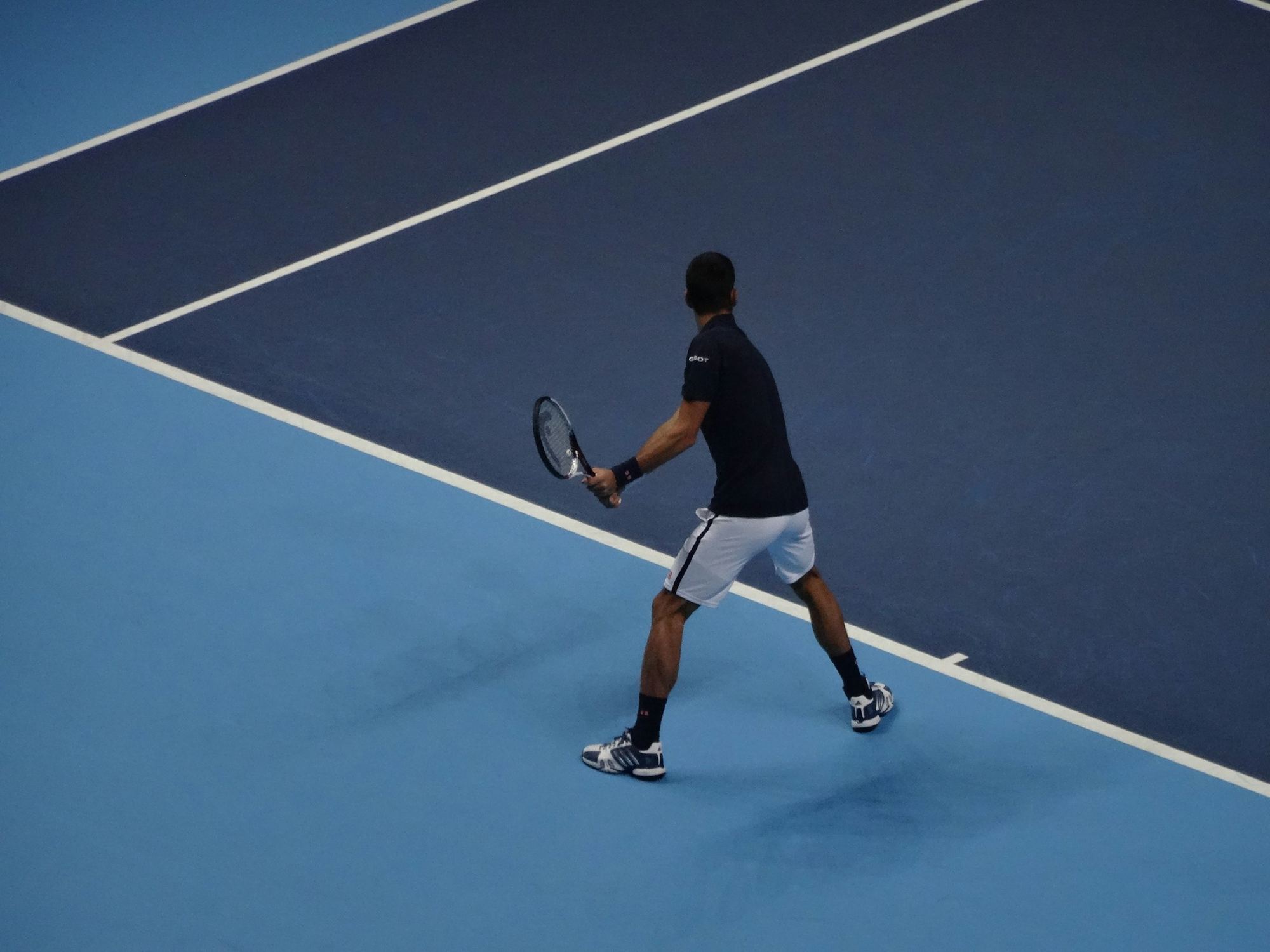 Tennis player hitting a backhand on a blue hard court, seen from above