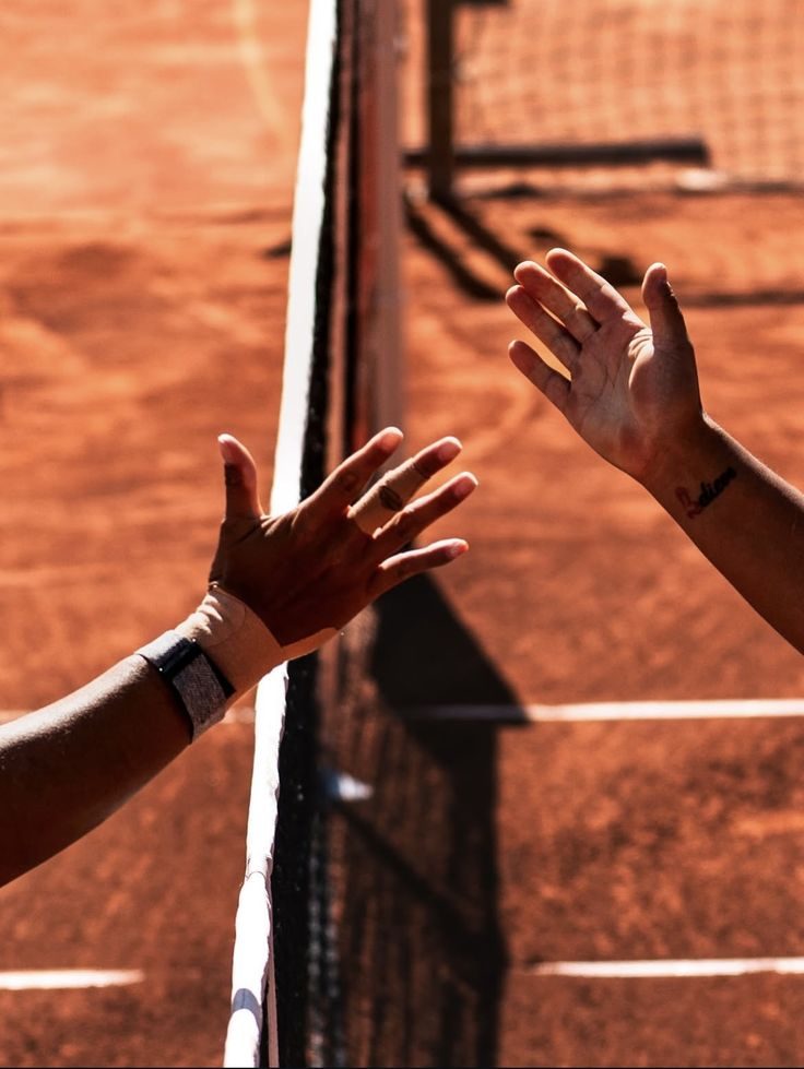 Two players shaking hands over the net on a clay court