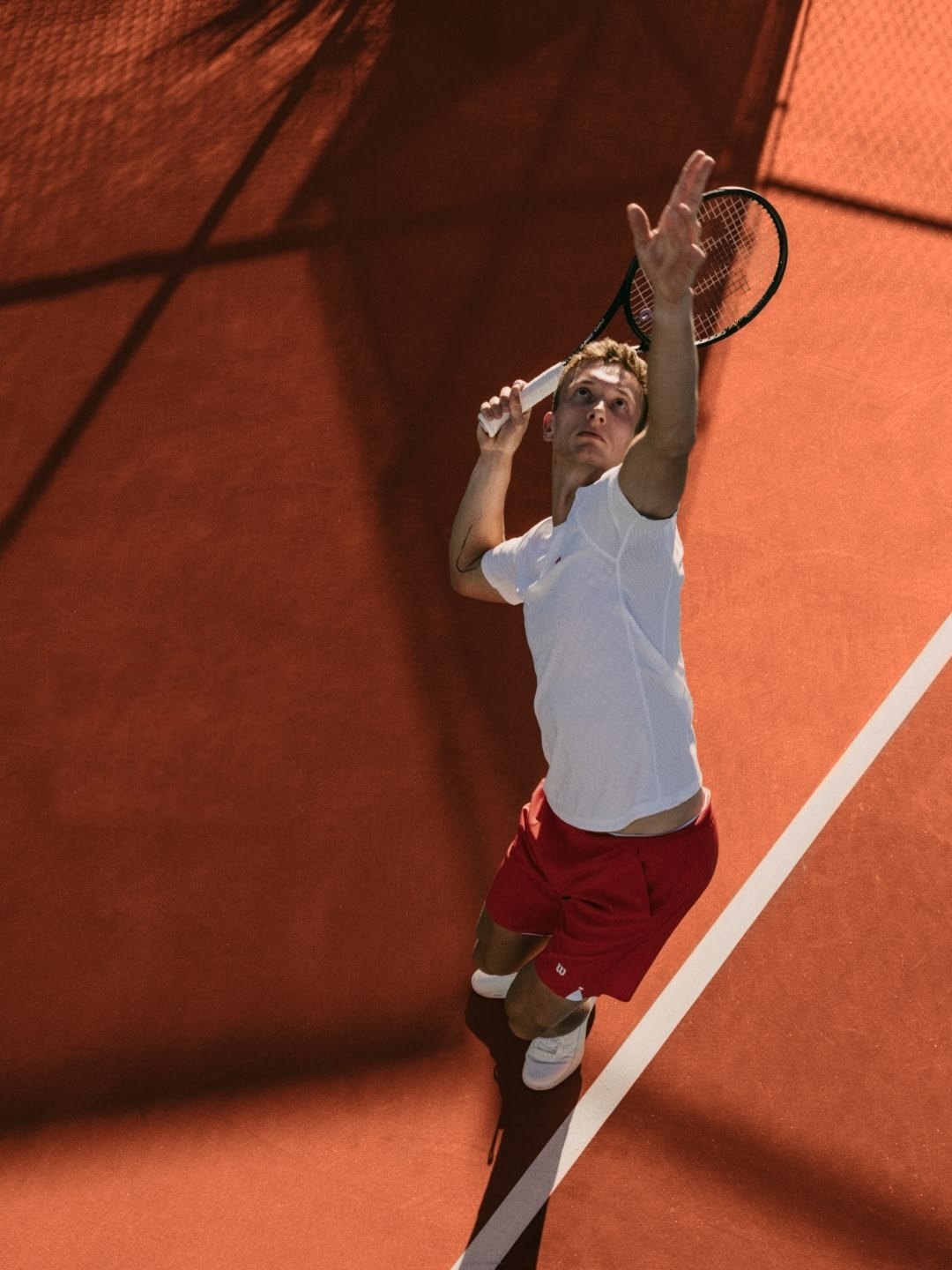 Tennis player serving on a clay court, seen from above