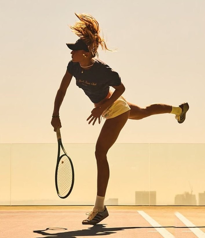 Tennis player finishing a serve on a rooftop court at sunset