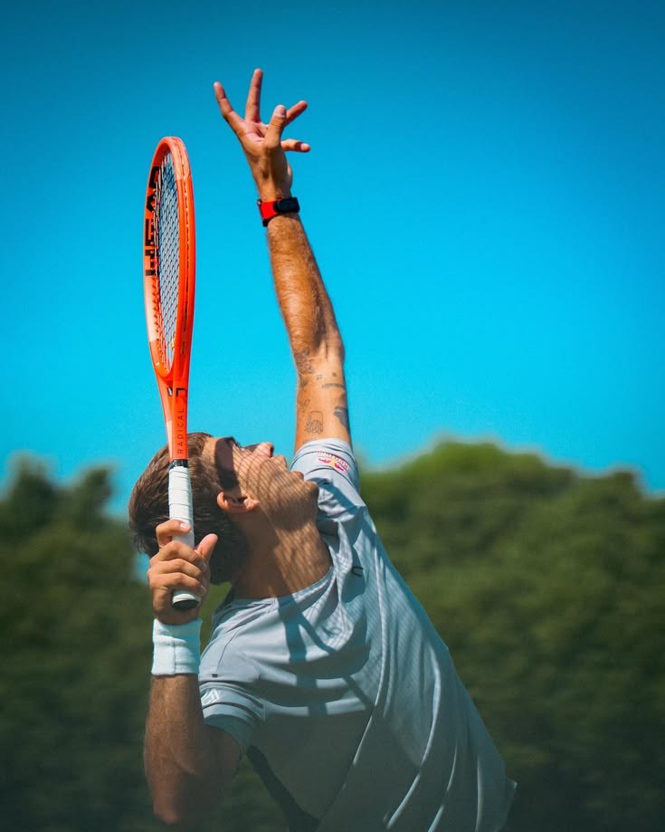 Tennis player reaching up into a serve under a blue sky