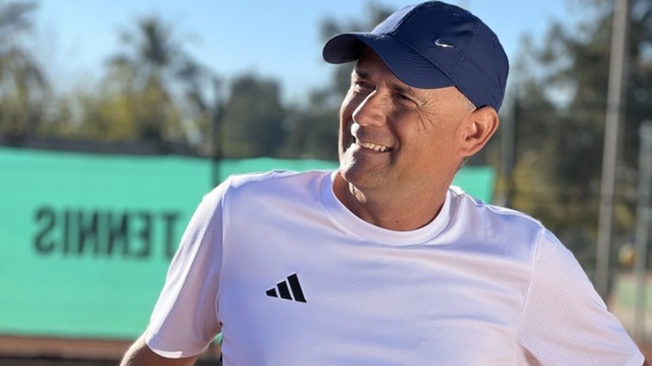 Smiling tennis coach in a cap at an outdoor court