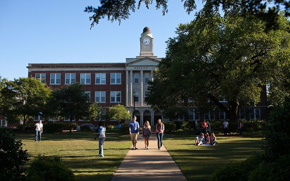 Nelson Hall, a red-brick building with a white columned entrance and clock tower, at the end of a tree-lined lawn with students on the Mississippi Christian University (formerly Mississippi College) campus in Clinton, Mississippi