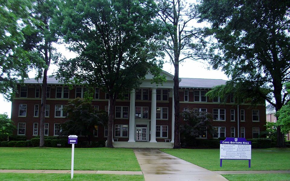 Cone-Bottoms Hall, a red-brick building with a white-columned portico, behind tall trees on Ouachita Baptist University&rsquo;s campus in Arkadelphia, Arkansas