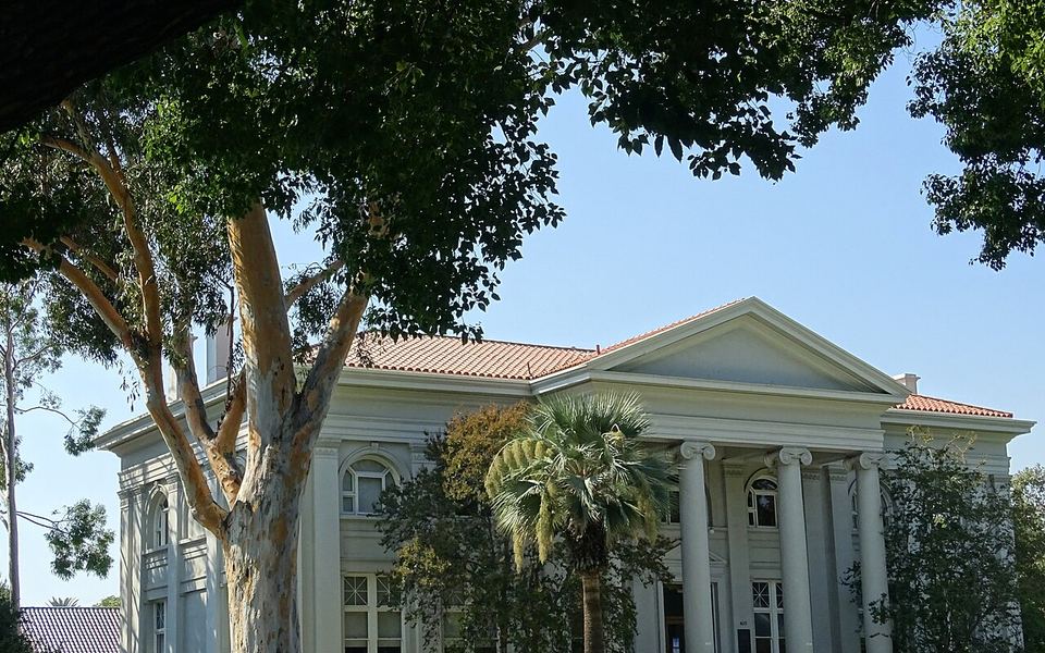 The Carnegie Building, a white neoclassical hall with Ionic columns and a red-tile roof, framed by trees and a palm on the Pomona College campus in Claremont, California