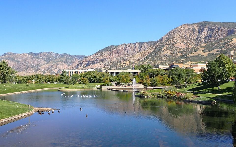 A pond with a fountain on Weber State University&rsquo;s campus in Ogden, Utah, with campus buildings and the Wasatch Mountains behind